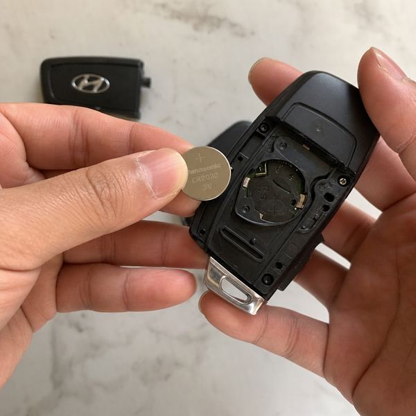 Close-up of hands replacing a small round battery inside a car key fob